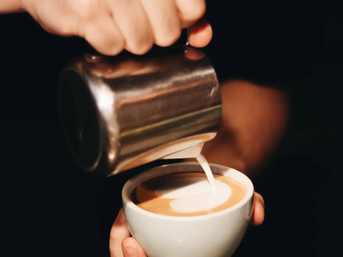 Milch wird für Latte Art in eine Kaffeetasse gegossen