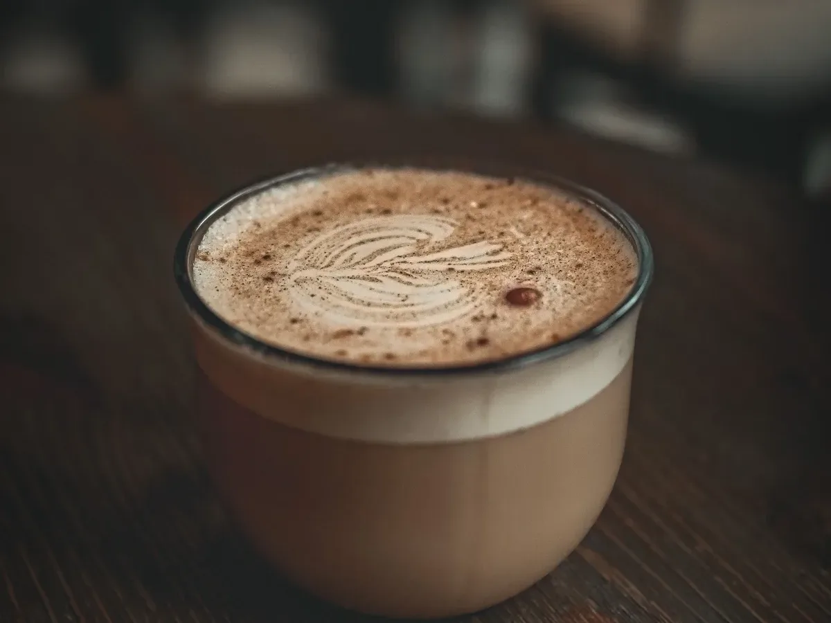 Detailaufnahme einer Kaffeetasse mit Latte Art auf einem dunklen Holztisch