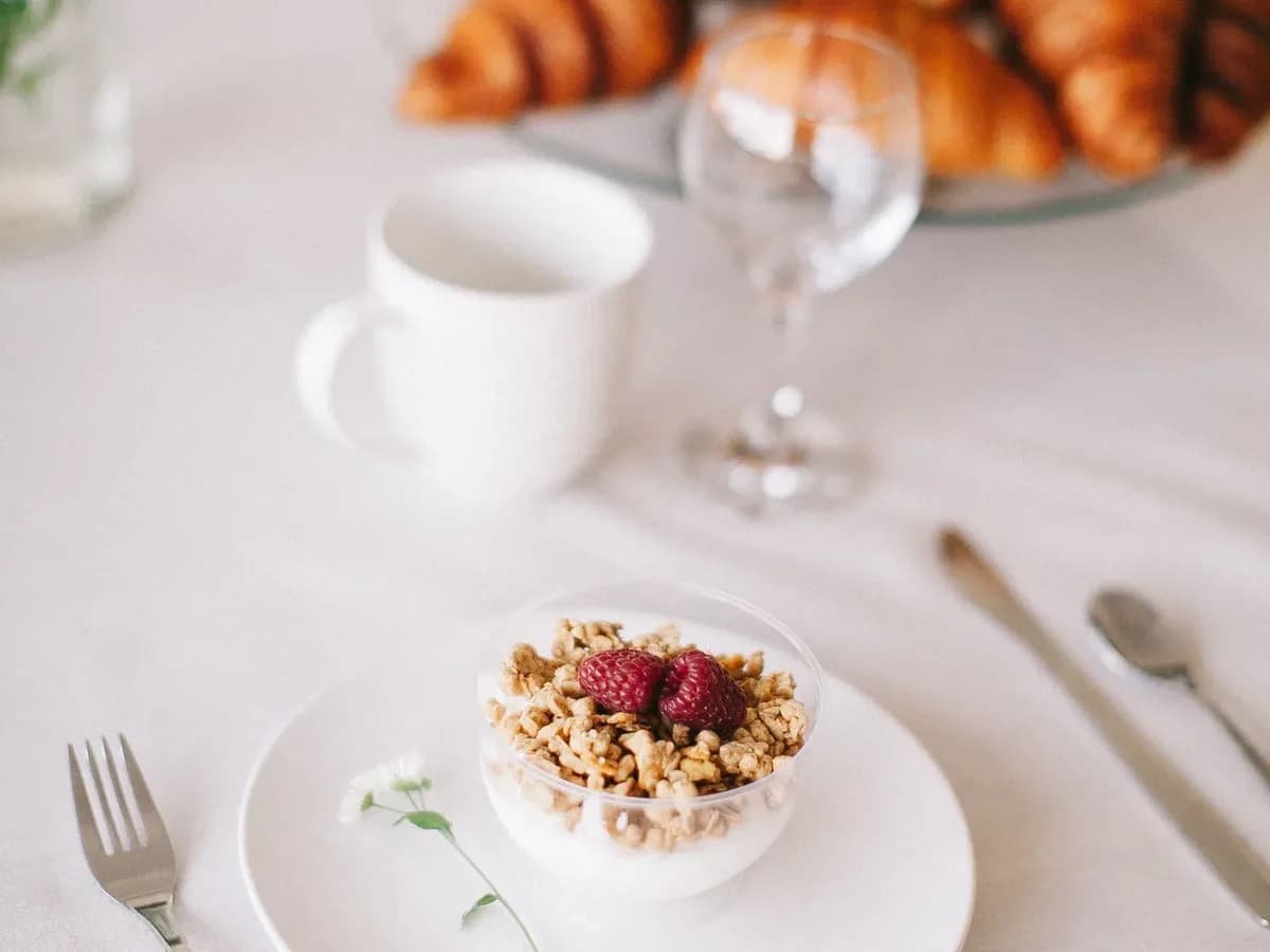 Frühstückstisch mit Croissants, Joghurt-Granola-Schale und Kaffeetasse